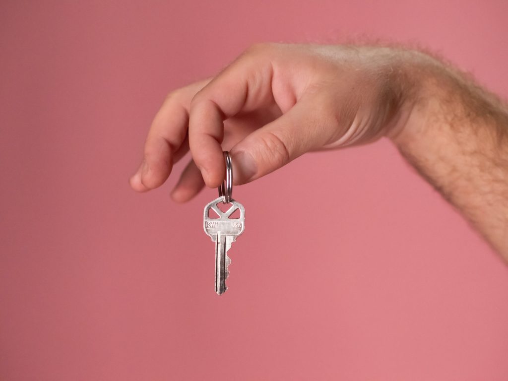 hand holding a key with his 2 fingers with the background color of pink