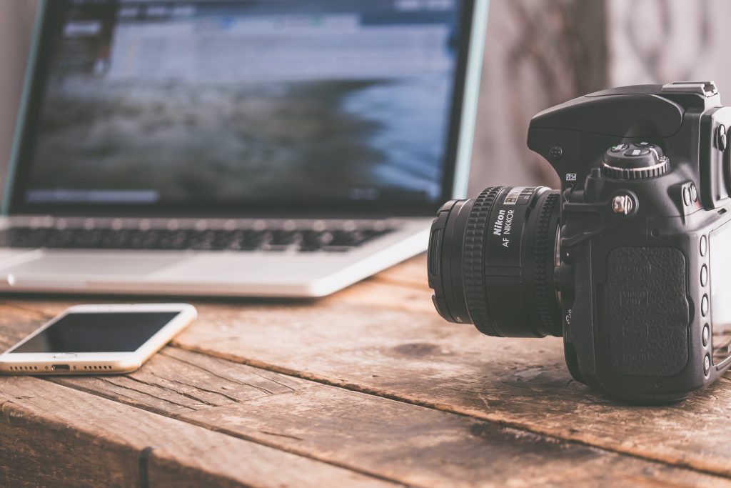 digital camera beside a laptop and a mobile phone