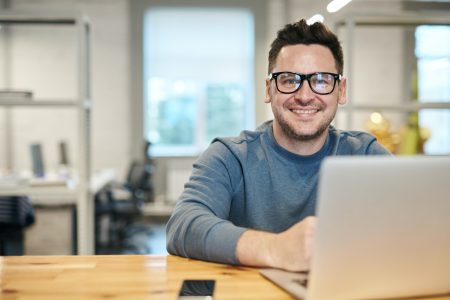 accountant with a smiling face that has his hands on top of a laptop