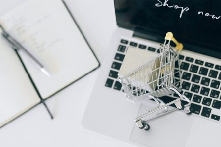 small shopping cart above a laptop with a notebook beside